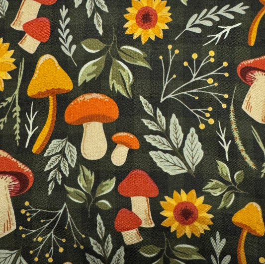 A close-up of a fabric pattern featuring a woodland theme with orange and red mushrooms, yellow sunflowers, green leaves, and delicate white botanical stems on a dark charcoal background.
