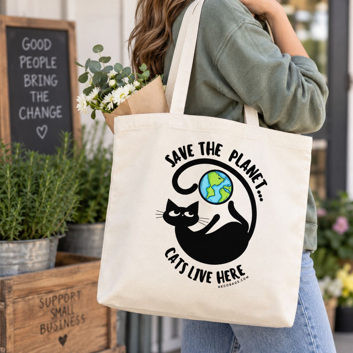 Woman carrying Save the Planet Cats Live Here canvas tote bag beside a black and white cat