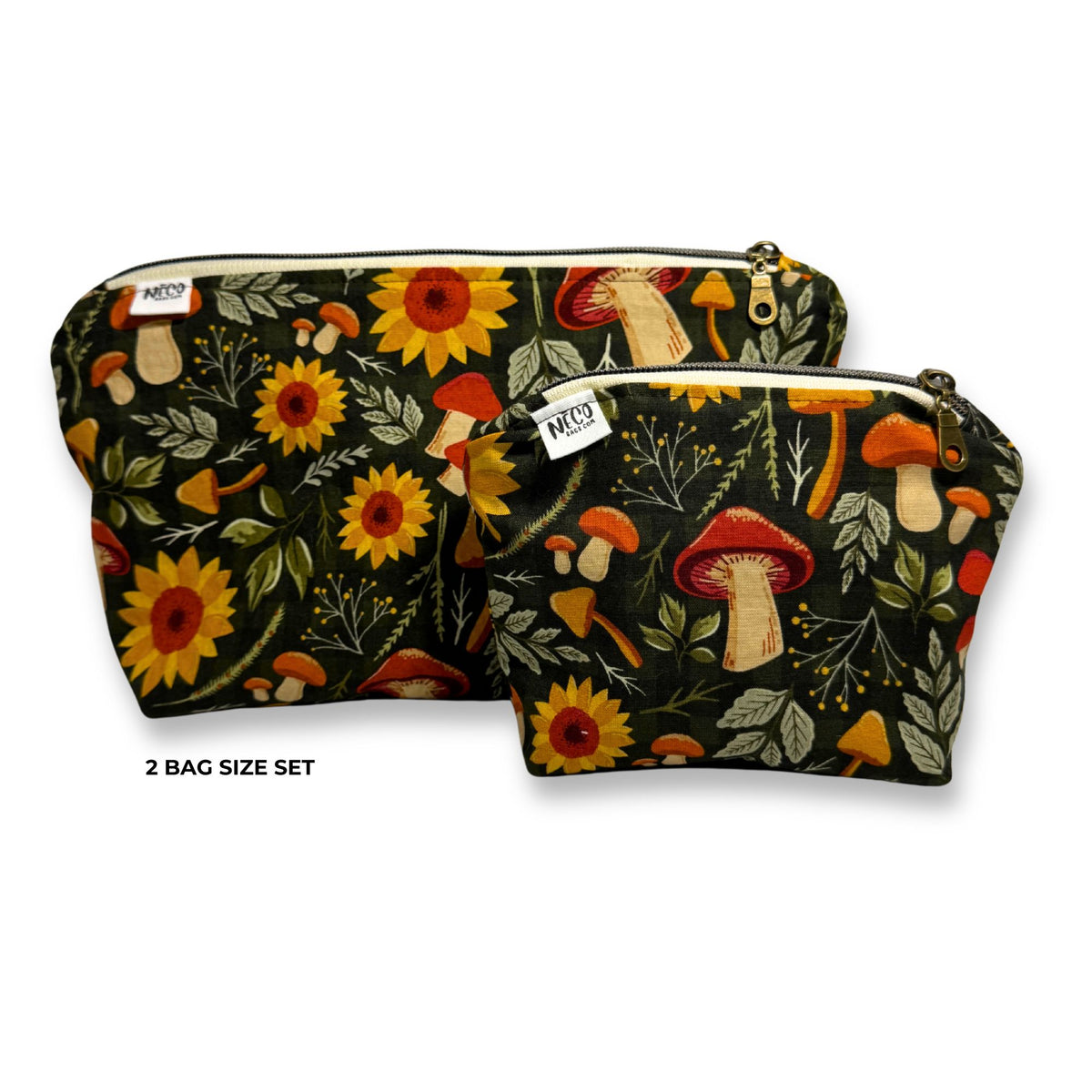 Two small zip pouches in a matching 2-pack size set, featuring a dark forest pattern with yellow sunflowers, red and orange mushrooms, and green leaves. The pouches have gold-tone zippers and a small white brand tag on the front. Machine washable and dryer friendly cosmetic toiletry bags