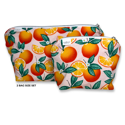 Two zippered pouches in a size set, featuring a vibrant orange and green citrus pattern on a light pink background. The pouches are displayed against a clean white background with a text overlay . reading '2 BAG SIZE SET'. Machine Washable Cosmetic Bags 