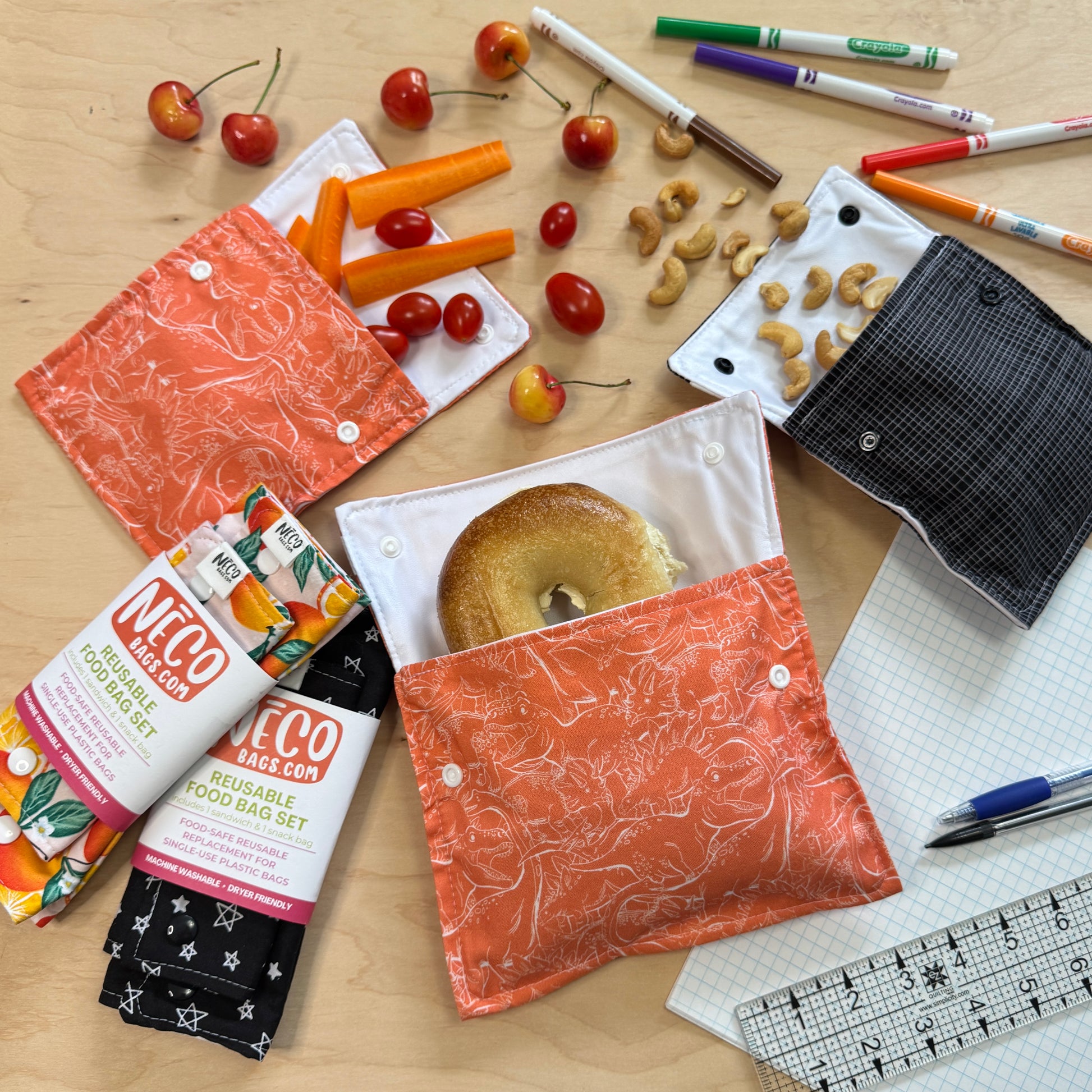 A flat-lay of cute snack and sandwich bags. Reusable food bag sets on a light wood surface, shown with snacks NECObags.com reusable food bag sets. 