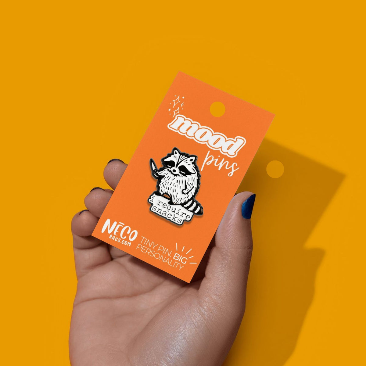 I Require Snacks raccoon enamel pin measuring 1.1 inches wide by 1.1 inches tall shown on display card