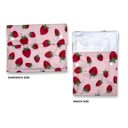 Two strawberry-print fabric pouches shown on a white background, labeled 'SANDWICH SIZE' and 'SNACK SIZE'. The food safe bags have a light pink background with cute red strawberries. Cute fun, and colorful machine washable food bags