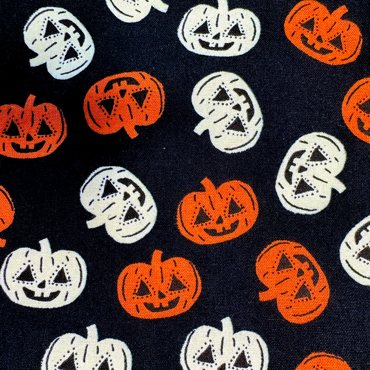 A close-up of a fabric pattern featuring orange and white jack-o'-lantern pumpkins on a black background.