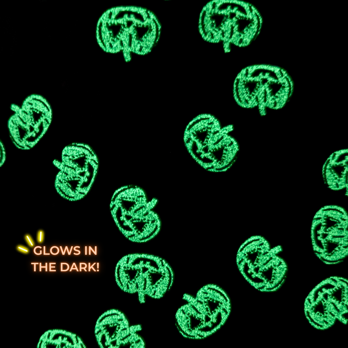 Black fabric pattern featuring glowing green jack-o'-lantern shapes and orange text that reads 'GLOWS IN THE DARK!'
