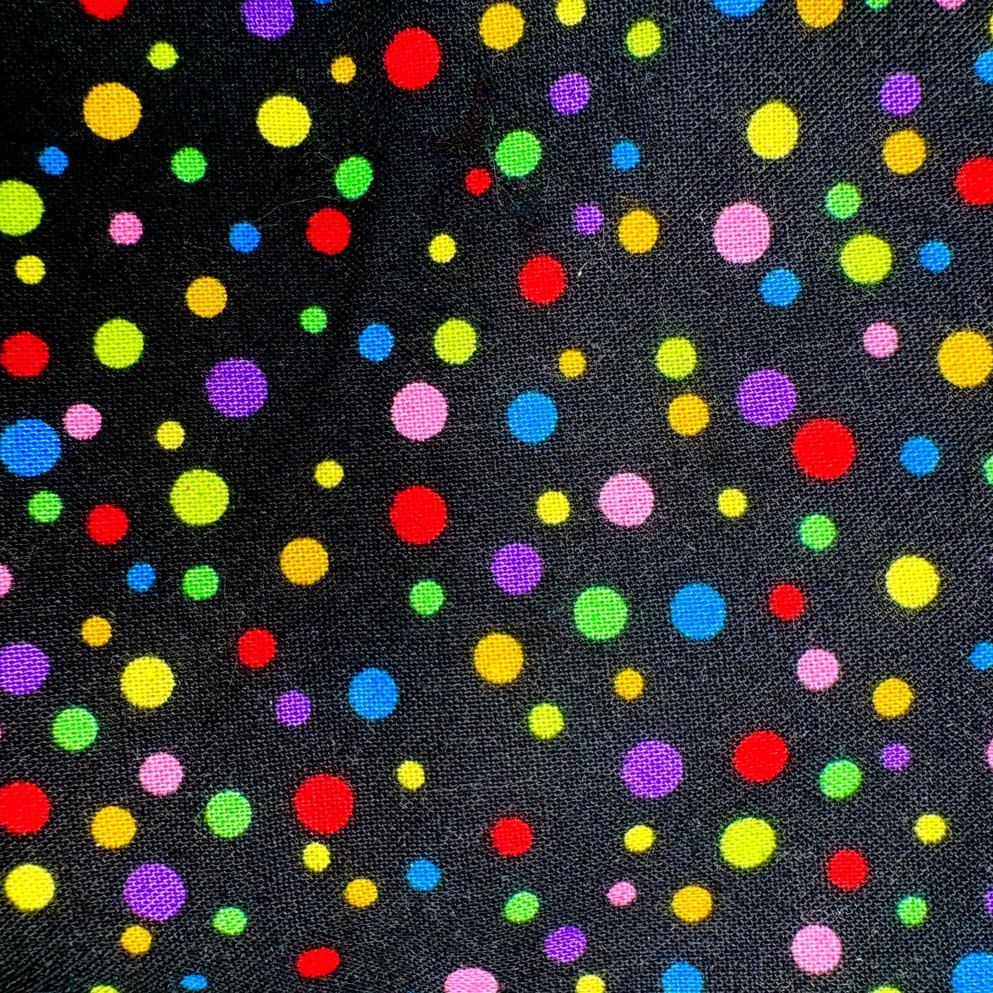 Black fabric with a colorful polka dot pattern featuring red, yellow, green, blue, pink, and purple dots of various sizes.