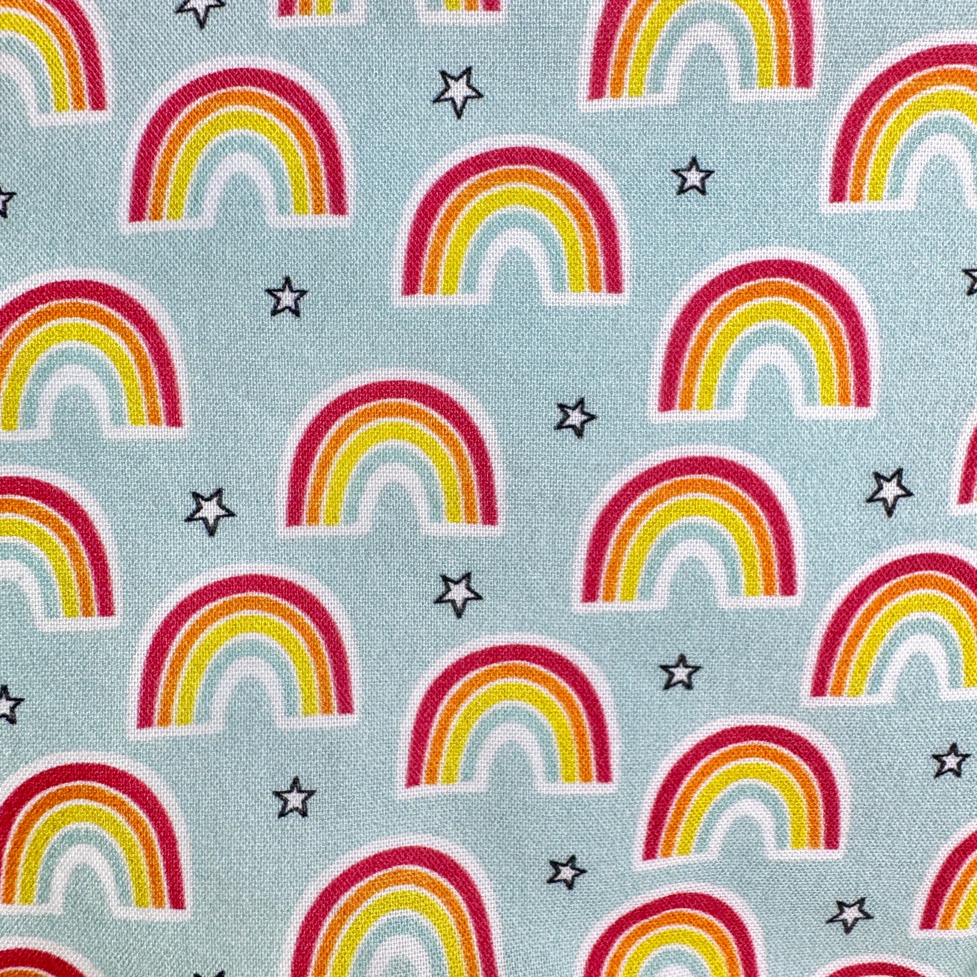 A close-up of a light blue fabric with a repeating pattern of colorful rainbows and small black outlined stars.