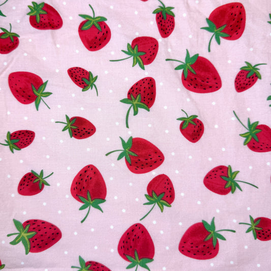 A close-up of a light pink fabric with a repeating pattern of red strawberries and small white polka dots.