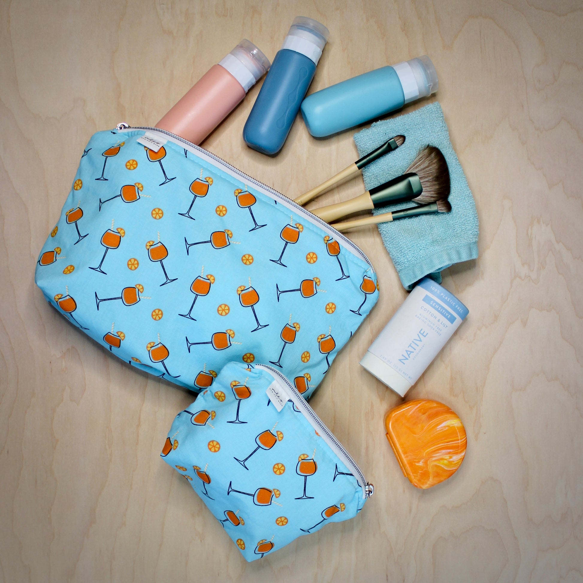 Two blue zippered bags with a leaf pattern, displayed alongside various personal items such as bottles and makeup brushes.